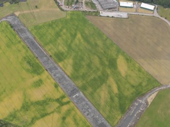 Oblique aerial view of the cropmarks of the ring ditch and the field boundaries at Castle Kennedy airfield, taken from the ESE.