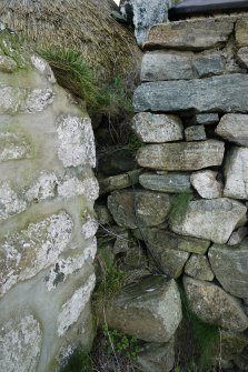 Detailed view of the junction between the East elevation of the thatched cottage at 13 Kilmoluaig, Tiree, and the adjoining building. Makeshift steps can be seen, which give access to the wallhead.