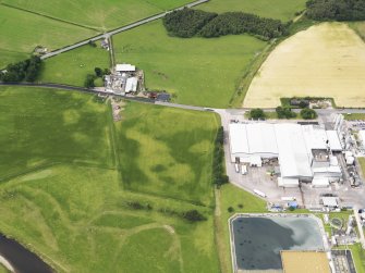 Oblique aerial view of the cropmarks of the barrow and possible field boundary with Priestdykes farmstead beyond, taken from the ENE.