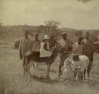 View of girl on donkey in Rhodesia, present day Zimbawe. 
Titled above image: 'Glen Lorne 1907. Rhodesia. Houseboy, Outside boy, Stable boy, Cook'. 
Titled below image: 'Neddy, Lorna, Walter, House boy'

