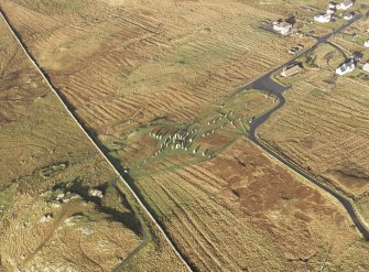 Oblique aerial view centred on the stone circle and stone row, the remains of the buildings and lazy beds at Calanais, taken from the SE.