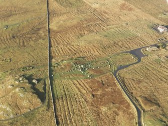 Oblique aerial view centred on the stone circle and stone row, the remains of the buildings and lazy beds at Calanais, taken from the ESE.