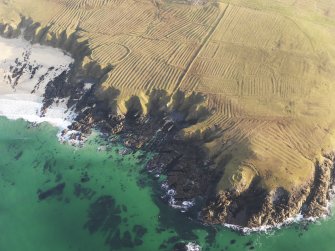 Oblique aerial view of the remains of the lazy beds, enclosures and head dyke at Carnan Thangadeir with Dun Mara in the foreground, taken from the NW.