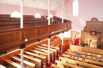 General view from rear gallery, looking along side gallery and down onto pews and central pulpit.