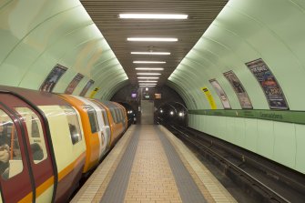 View looking along the island platform of Cowcaddens subway station, towards the tunnel openings and fire exit, with a train waiting at the Outer Circle platform