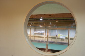 Interior. Detail of porthole within central corridor wall, looking into carpet bowls hall.