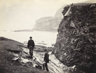 View of rock formations and surrounding beach, including two figures, on the beach of Kilchattan, Colonsay. 
Titled: '149. Behind Kilchattan, Colonsay.'
PHOTOGRAPH ALBUM NO 186: J B MACKENZIE ALBUMS vol.1