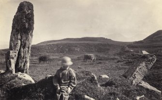 View of figure in front of one of the two standing stones, originally thought to have been part of a stone circle known as "Fingal's Limpet Hammers," at Lower Kilchattan, Colonsay.
Titled: '104. Above the XXX at Scalasaig on the road to Kiloran.'
PHOTOGRAPH ALBUM, NO 186: J B MACKENZIE ALBUMS vol.1