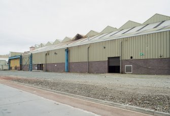 Central Yard, south wall, west end. General view of workshop from South East showing the remnants of the Travelling electric crane gantry and uprights (painted blue, left) from 1906 when this area was an open yard. It was later covered over and became the covered steel stockyard where the plate metal was kept out of the elements. This shed has since been demolished (in 2013), revealing the remnants of the original layout. The saw toothed roof of the original 1906 boiler shop is visible behind (latterly the Plate Preparation Shop).