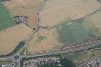 Oblique aerial view of the cropmarks of the enclosure with Easter Broomhouse farmstead beyond, looking SSW.