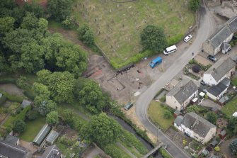 Oblique aerial view centred on the Glasgow University excavations on the edge of the churchyard, looking SSW.