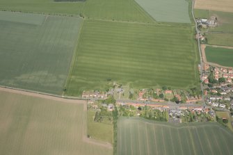 Oblique aerial view of Athelstaneford village with the cropmarks of possible buildings and road adjacent, looking N.