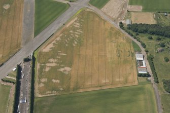 Oblique aerial view of East Fortune Airfield, First World War airship shed base under modern agricultural buildings, a military workshop building, and cropmark features relating to airship station, looking SW.