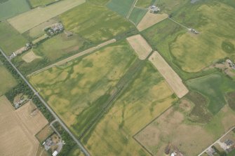 Oblique aerial view of the cropmarks of the possible round house, sunken floored building, field boundary, rig and pits, looking NE.