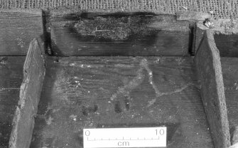 Binnacle (DP96/004), detail showing the central compartment. Note the burnt hole at the top, and the patch used to repair it. Four small scorch-marks can be seen on the plank below. Scale in centimetres. (Colin Martin)
