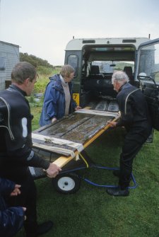 Graham Scott (left), Dr Paula Martin and Dr Colin Martin carefully load a wooden panelled door (DP00/146) on a lifting-frame to which it is secured with bandages into a Land Rover for transport to wet holding-tank. Once inside it will be covered with wet towels. (Edward Martin)