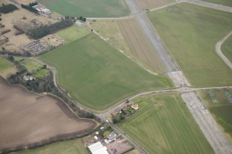 Oblique aerial view of a circular cropmark, part of the First World War airship station gas works, and East Fortune farm, looking ESE.