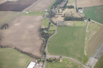 Oblique aerial view of a circular cropmark, part of the First World War airship station gas works, and East Fortune farm, looking ESE.