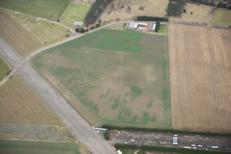 Oblique aerial view of the First World War airship shed base under modern agricultural buildings and a military workshop building to N, looking NNW.