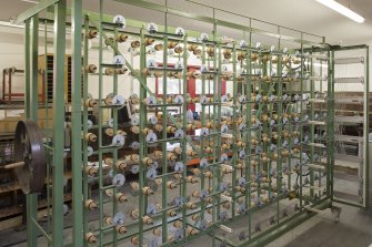 Interior. New weaving shed. View of warping or beaming machine. This takes single yarn strands from many bobbins on the frame and winds under tension onto a beam ready for weaving.