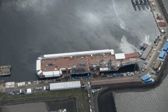 Oblique aerial view of the Main Basin, Rosyth Naval Dockyard showing the construction of an aircraft carrier, looking SE.