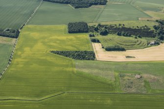 Oblique aerial view of the cropmarks of the ring ditch houses and the pit-defined boundary with The Chesters fort beyond, looking S.