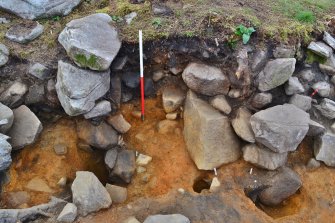Dun inner wall face (large stone in centre of image) and build-up of material against the inner wall on the south side of the entrance passage; east posthole in entrance passage (right) and interior posthole in dun courtyard (left) with small stakehole between, Comar Wood Dun, Cannich, Strathglass