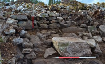 East facing dun outer wall and blocked passage (marked by upright scale pole); large recumbent boulder in front may have formed part of an exterior wall, Comar Wood Dun, Cannich, Strathglass