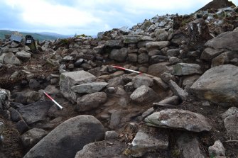 Mid-excavation image after initial clean-back showing blocked passage in the outer wall (top centre) and possible external wall base (left centre); image shows large displaced slab in left foreground, which may be a displaced slab from the external wall, Comar Wood Dun, Cannich, Strathglass