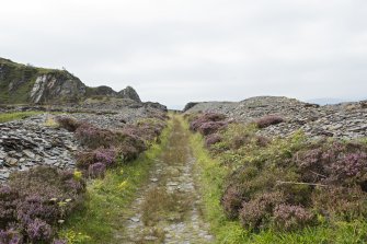 Slate spoil heaps either side of track leading to break in wall, view from east