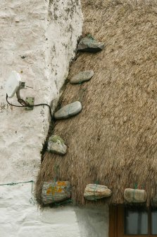 Detail of stone weights on thatch beside chimney breast; thatched cottage Reumisgarry, North Uist.