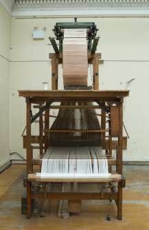 Interior. General view. Jaquard loom in gallery area. The warp beam is clearly visible as is the jacquard device above the loom. The holes and blanks on the cards allow the hooks in the frame to select or not select threads to create the complex patterns in the cloth