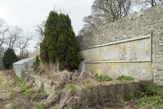 General view of remains of garden building with greenhouse behind.