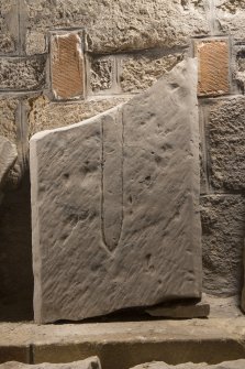 Obliquely lit view of medieval cross slab fragment.
