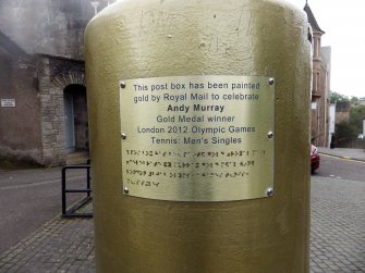 Close up view of the plaque on the side of the post box but also the graffiti scratched into the paint above it.