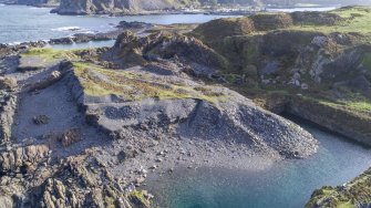 Oblique aerial view of quarry An Toll Mar Luaty showing the slate waste dumped into it, possibly from the re-working phase of Hill/ Windmill Quarries in the early 20th century; west coastal quarrying evidence and sea erosion of slate waste