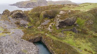 Oblique aerial view of An Toll Mar Luaty Quarry with remains of associated forge building and engine house with later slate waste tipping in the flooded quarry