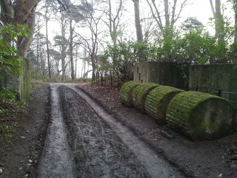 Looking E is a horizontal rail and linked cylinder type of road block which cuts through a line of anti-tanks blocks. It comprises two large concrete blocks on either side of the road. The N block has slots and the S block has holes into which metal rail were placed. Four concrete drums which lie on the S side of the road, would have been rolled below the rails. Barbed wire would have been strung across and around the road block.