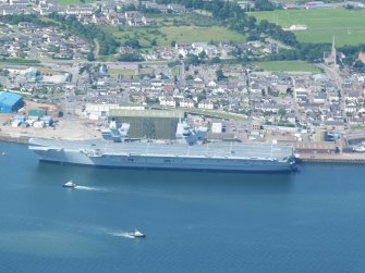 Oblique aerial view of west part of central Invergordon, with aircraft carrier at berth.