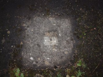 The stump of a mooring bolt at the centre of a cement filled square socket set in the floor of a hangar