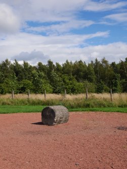 View from the N of a fluted cast concrete drum (possibly an anti-tank obstacle) displayed in the centre of the circular area of gravel modelled on a barrage balloon cradle