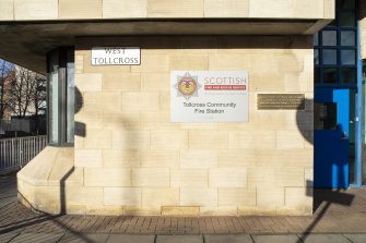 View of south facade on West Tollcross showing street sign, station plaque and memorial plaque to Firefighter Ewan Williamson.  From south west.