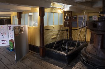 Interior. Gun Deck, astern. View towards light well for officers' cabin and mess area on Lower Deck and access stairs to Lower Deck. Capstan (earlier) on right