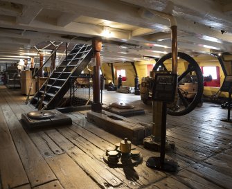 Interior. Gun Deck, midships looking towards starboard side. Pump in forground and navel or hawse pipes visible. Stairs to Upper Deck