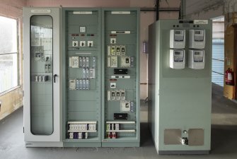 Interior. Carsfad Hydro Electric Power Station, Turbine House. Operating Room, first floor adjacent to Loading Bay (roller shutter visible on right). DC Board (left) and Metering Board (right).