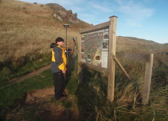View from the S of Alan Kilpatrick examining the Kincraig Battery notice board  at the foot of Craig Heugh (NT 47280 99926) 