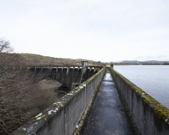 Carsfad Dam. East side of walkway on top of the dam with outlet needle valve house. Carsfad Reservoir is on the right