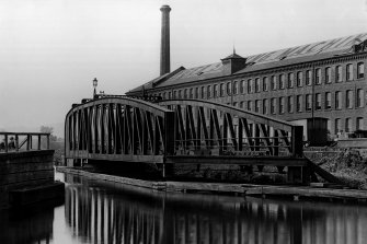 View of the railway bridge over the Forth and Clyde Canal at Kilbowie in the open position, photographed in the 1930s. Part of the Singer Sewing Machine factory is visible in the background.
