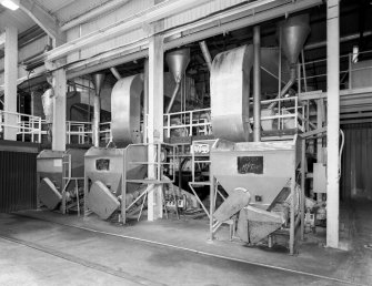 View of three of six Sodium Alginate drum driers, with feed hoppers in foreground.  The Sodium Alginate is milled after leaving the hopper, and is then blown into the revolving drum driers, which are supplied with steam-heated hot air