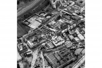 Oblique aerial view showing Canongate across centre of photograph, Calton Burial Ground at bottom, Abbey Strand to left, Meadow Flat Gas Holder at top and Cowgate heading to right